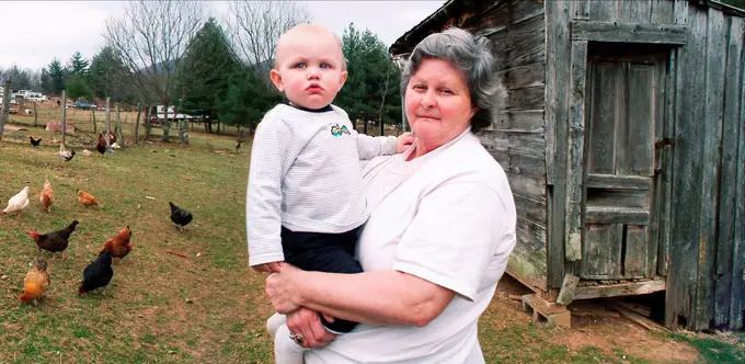 Grandmother carrying grandson near chicken coop on farm