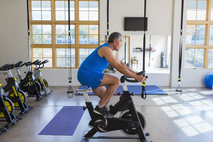 Mixed Race man riding stationary bicycle in gymnasium