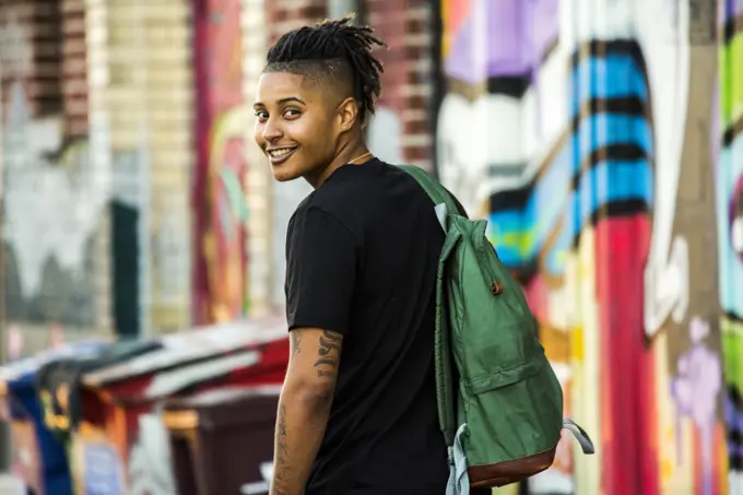 Portrait of smiling androgynous Mixed Race woman near on graffiti wall