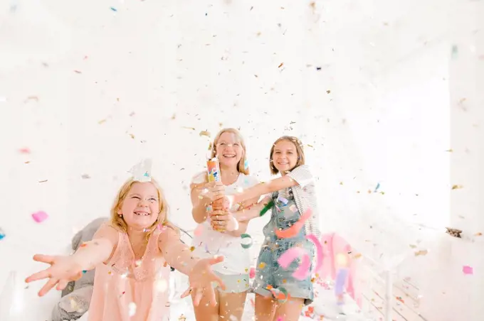 Smiling Middle Eastern girls throwing confetti in bedroom