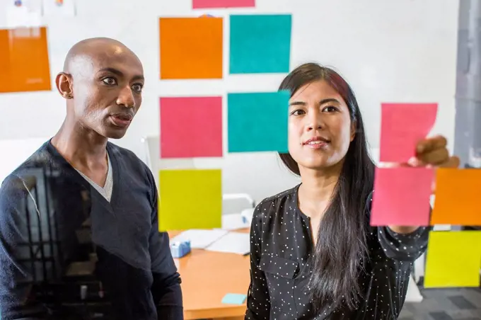 Woman and man reading adhesive notes in office