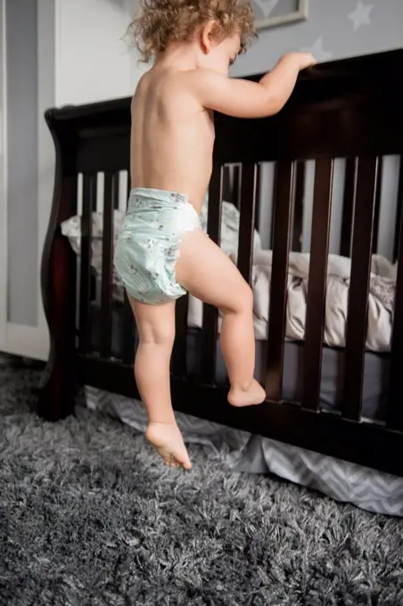 Caucasian boy wearing diaper climbing on bed frame