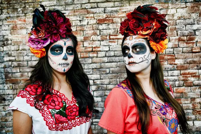 Women near brick wall wearing skull face paint