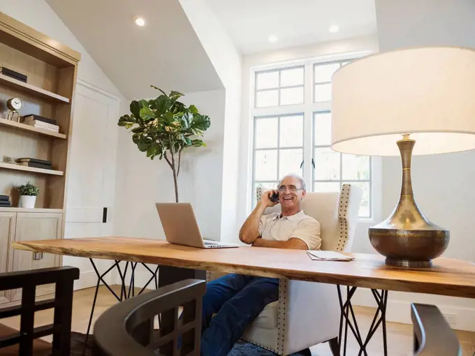 Caucasian man talking on cell phone in home office