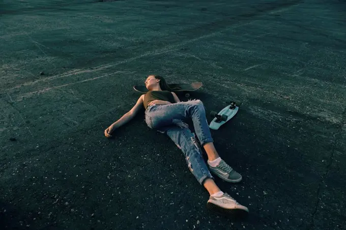 Caucasian teenage girl laying on pavement with head on skateboard