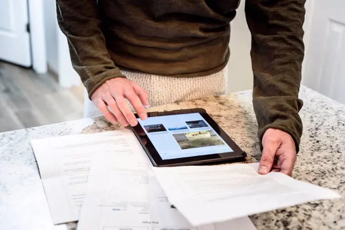 Caucasian man using digital tablet and holding paperwork