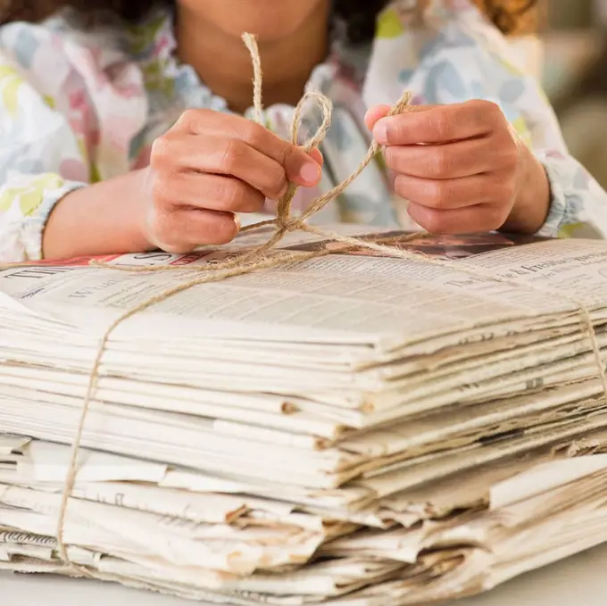 Mixed race girl tying bundle of newspapers