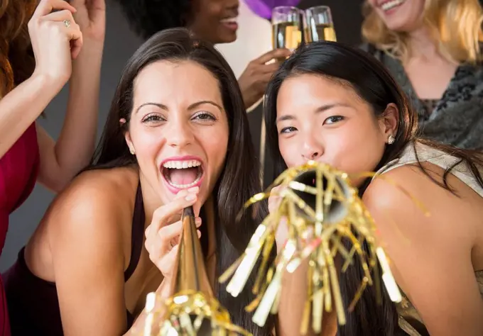 Smiling women blowing party horns at party