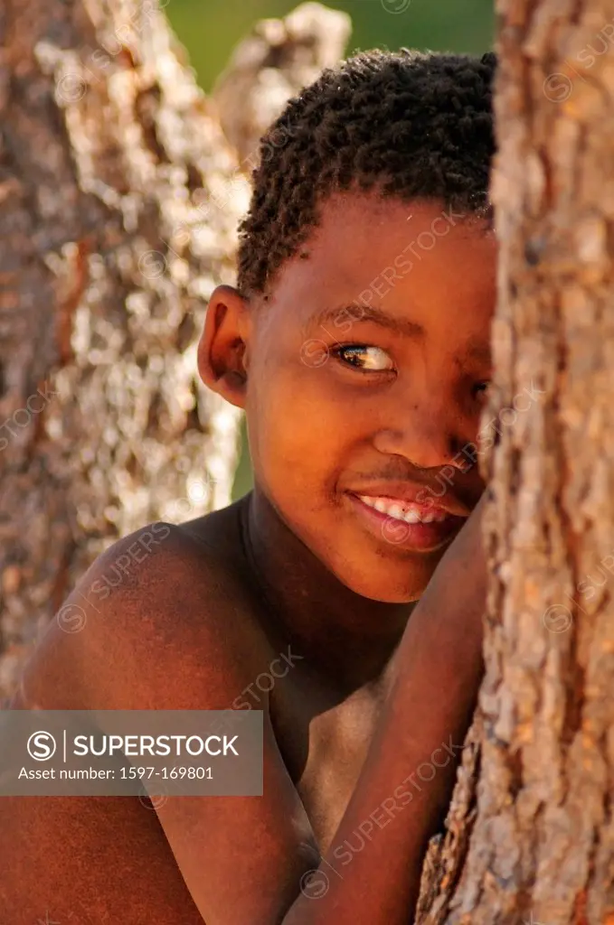 Africa, Bushmen, Namibia, Portrait, behind tree, boy, child, clan, hiding, hunter, gatherer, natural, nomad, primitive, smiling, tribe, vertical