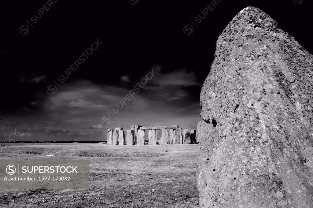 The heal stone with the rest of Stonehenge in the background and behind that Salisbury Plain at the summer solstice