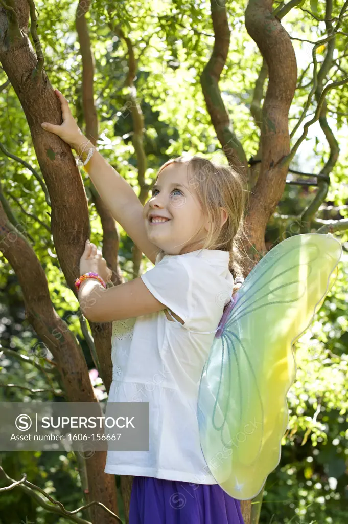 Little girl with butterfly wings ready to climb a tree, smilling