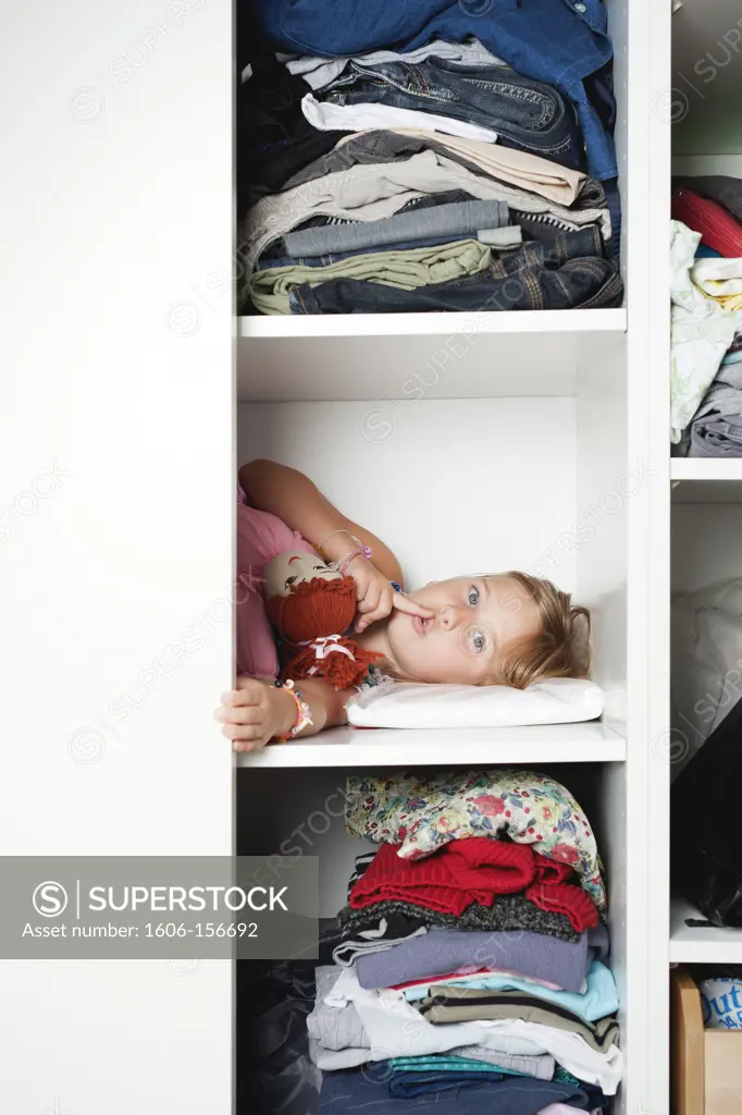 Girl hidden in a closet, making the sign ""silence"" with her finger on the lips