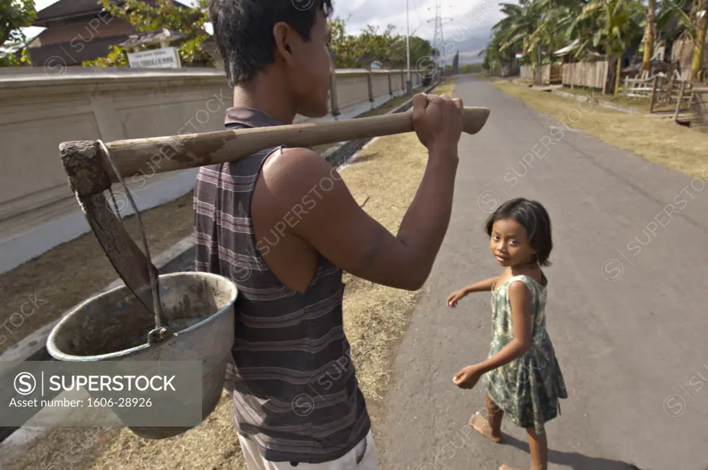 Indonesia, Bali, Gilimanuk, man walking, holding pickaxe and bucket, girl turning round