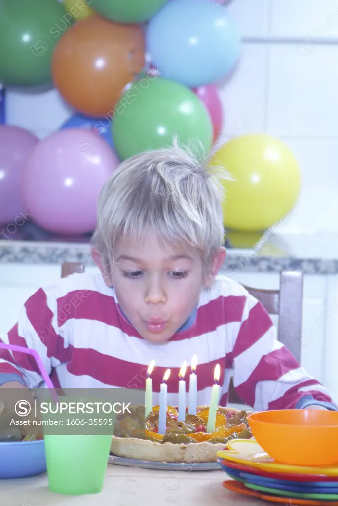 Boy blowing out candles, birthday cake, coloured plates, baloons