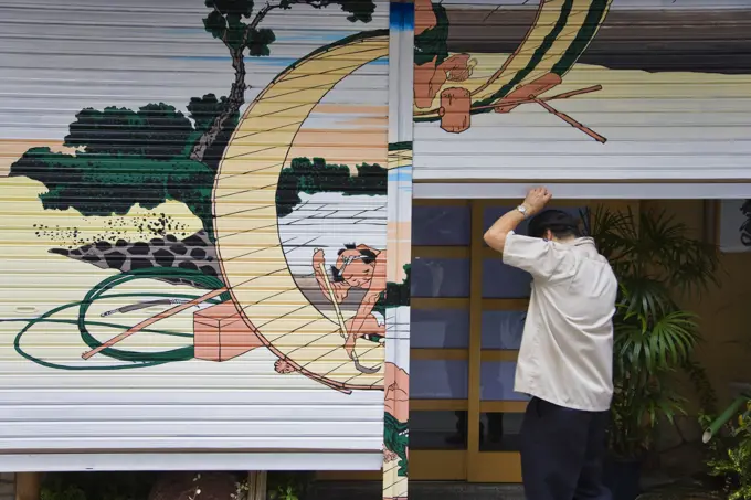 The owner opens the shutters of his traditional Japanese restaurant that are decorated with a Hokusai woodblock print in the Nihonbashi district of central Tokyo, Japan.