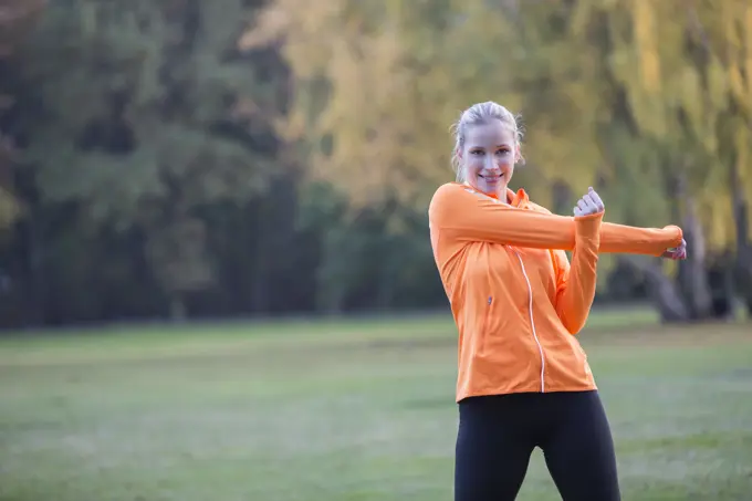 Pretty blonde woman stretching in park and smiling at camera