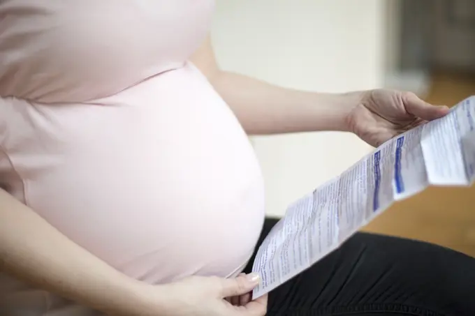 Close up of belly of a pregnant woman looking at a notice of a drug.