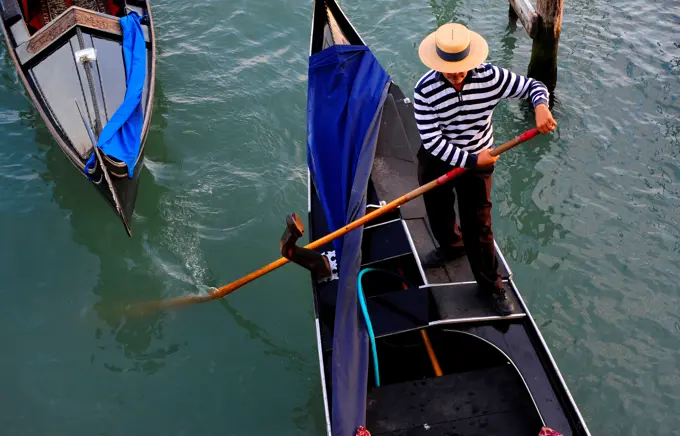 Gondolier Rowing A Gondola On Canal In Venice, Italy, Europe