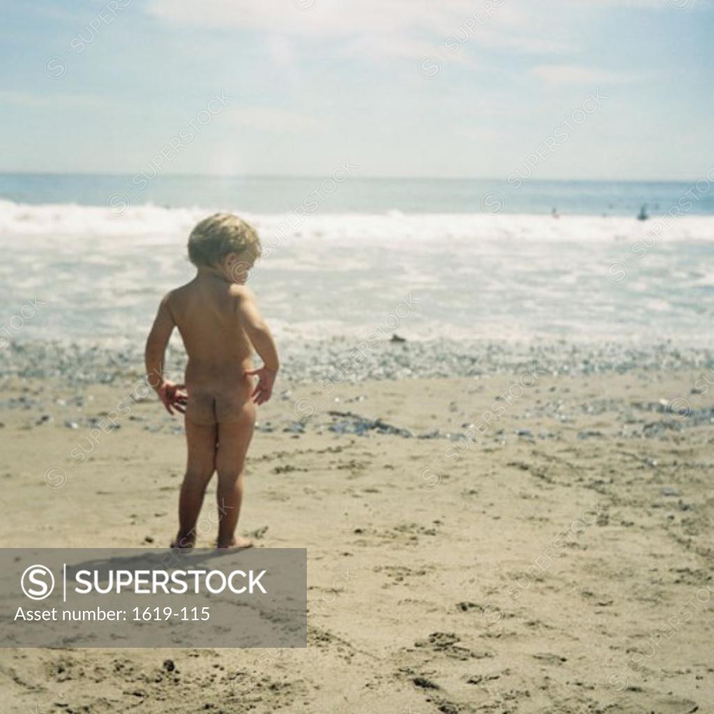 Rear view of a naked boy standing on the beach - SuperStock