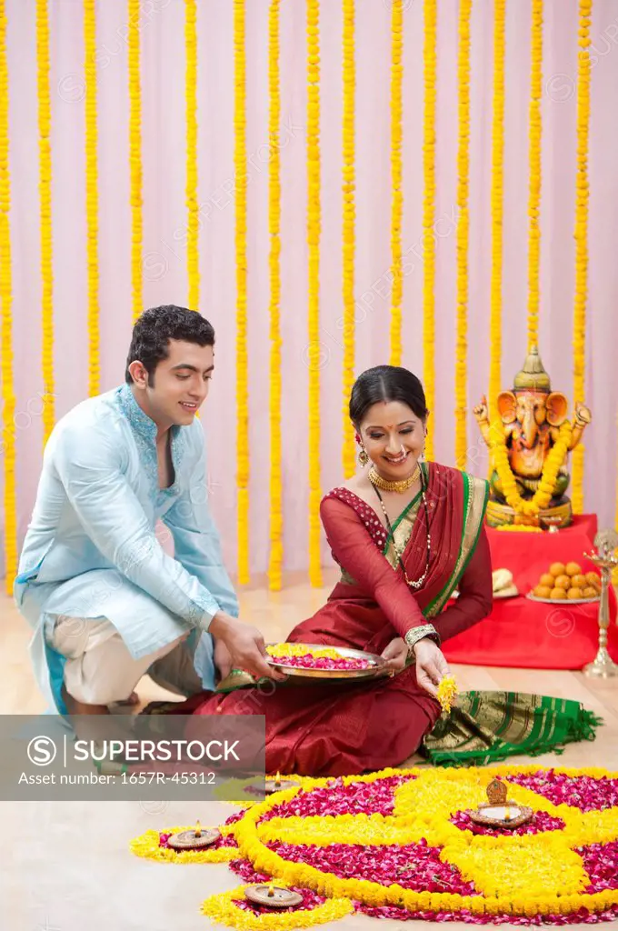 Maharashtrian couple making flower rangoli during ganesh chaturthi festival