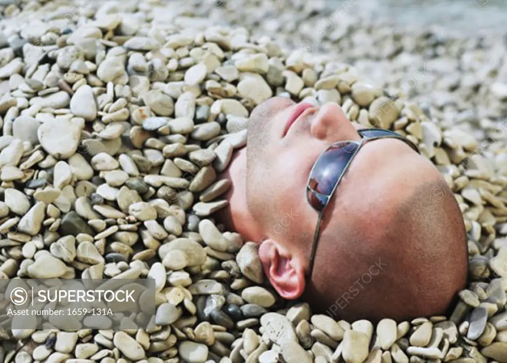 Close-up of a young man buried in pebbles on the beach