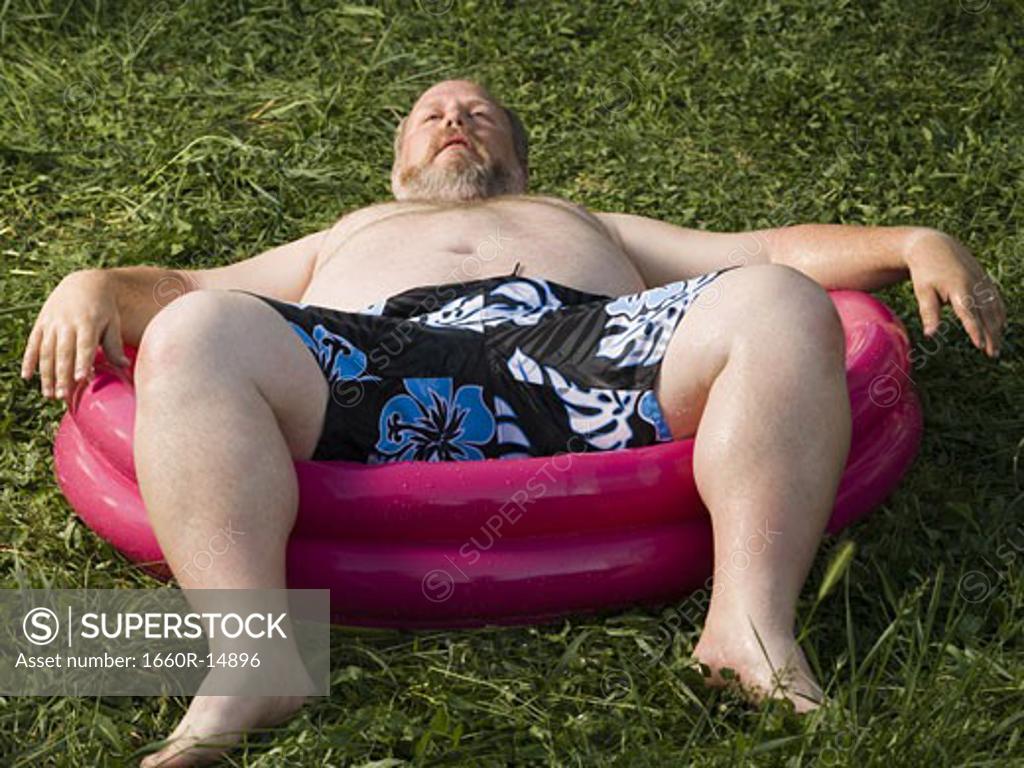 Overweight man in inflatable wading pool - SuperStock