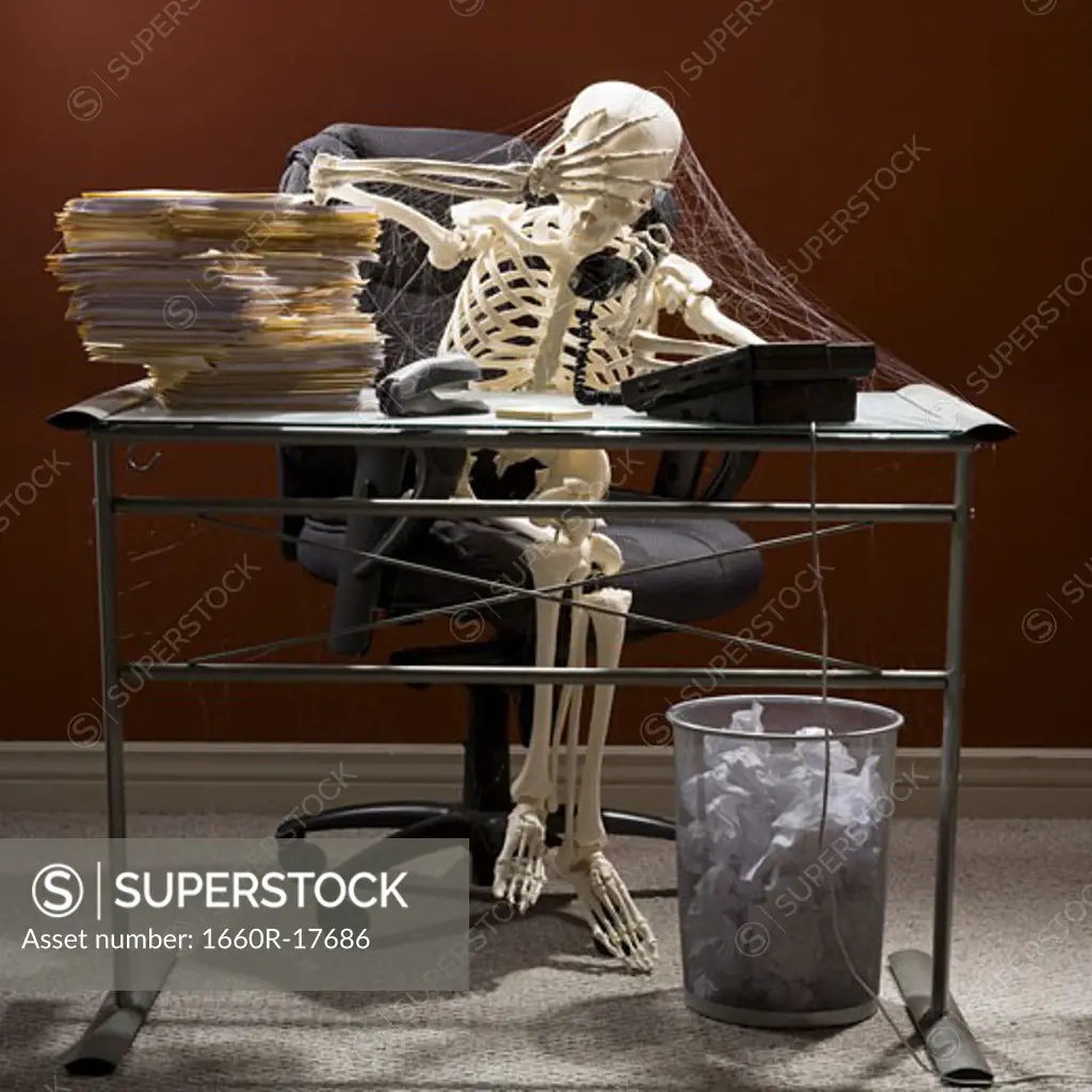 Skeleton sitting at desk talking on telephone with webs and stacks of paperwork