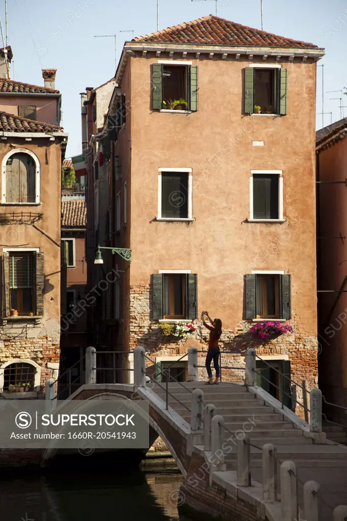 Italy, Venice, Woman standing on arch bridge and photographing italian houses