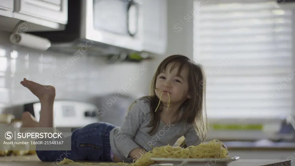 Naughty messy girl laying on kitchen counter eating plate of spaghetti