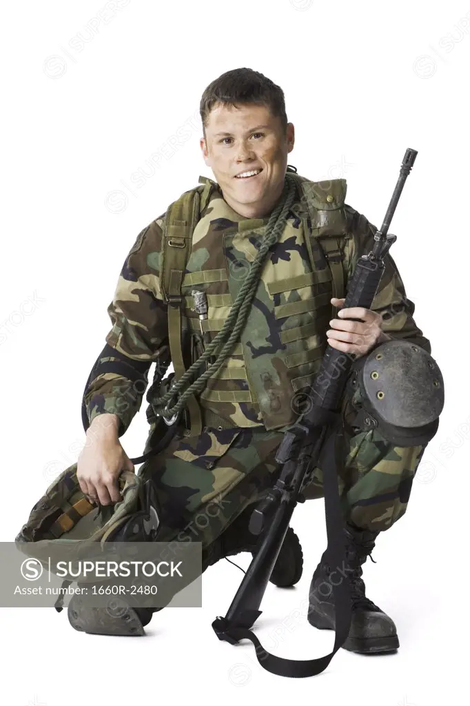 Portrait of a soldier crouching and holding a rifle and a helmet