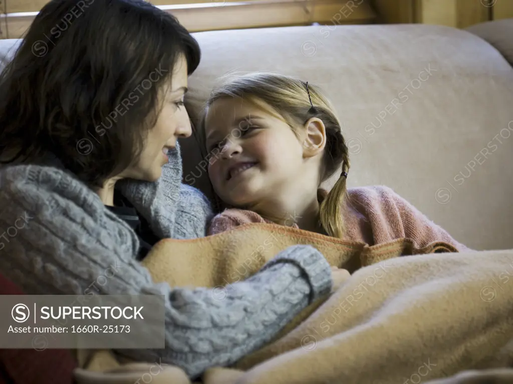 Woman with young girl snuggling on sofa