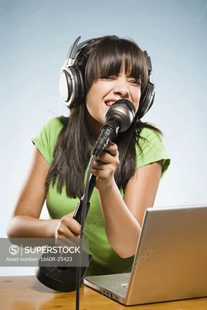 Young woman recording into a microphone with headphones and a laptop