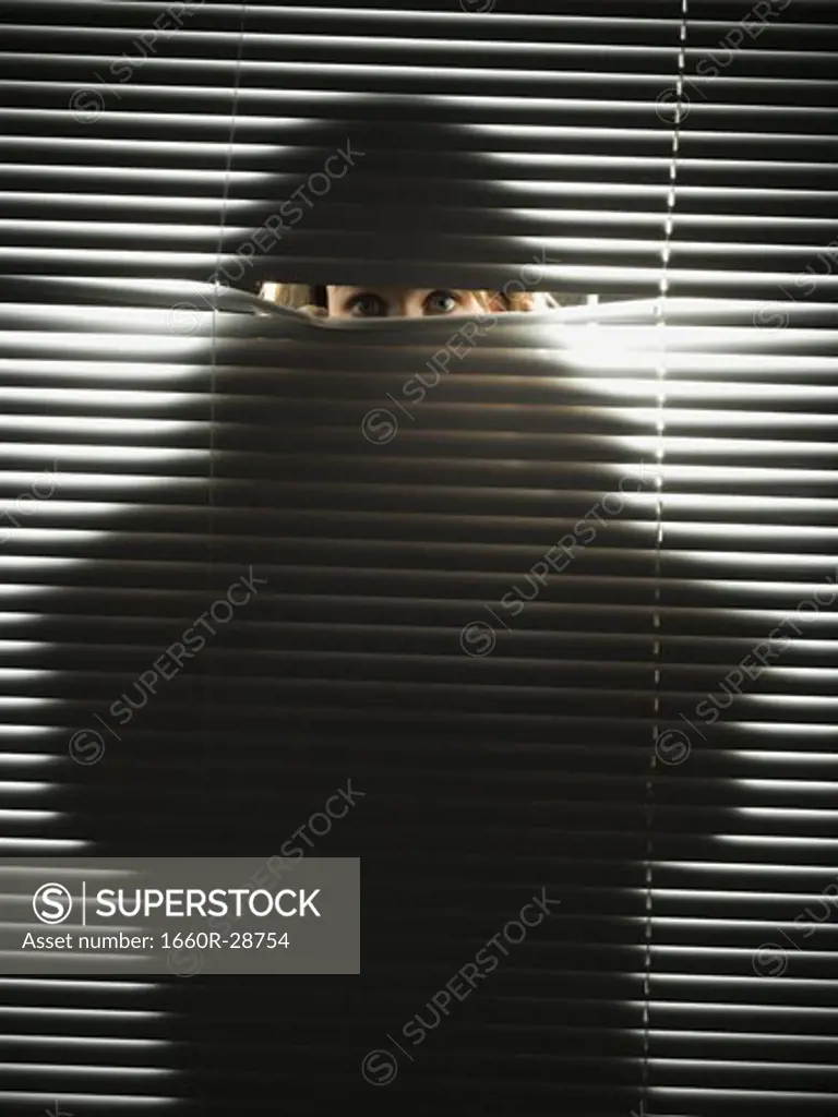 Woman peeping through horizontal blinds