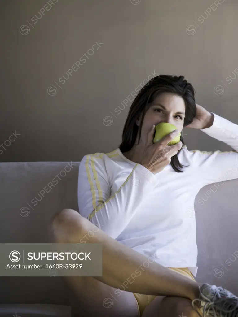 Woman sitting on sofa eating green apple