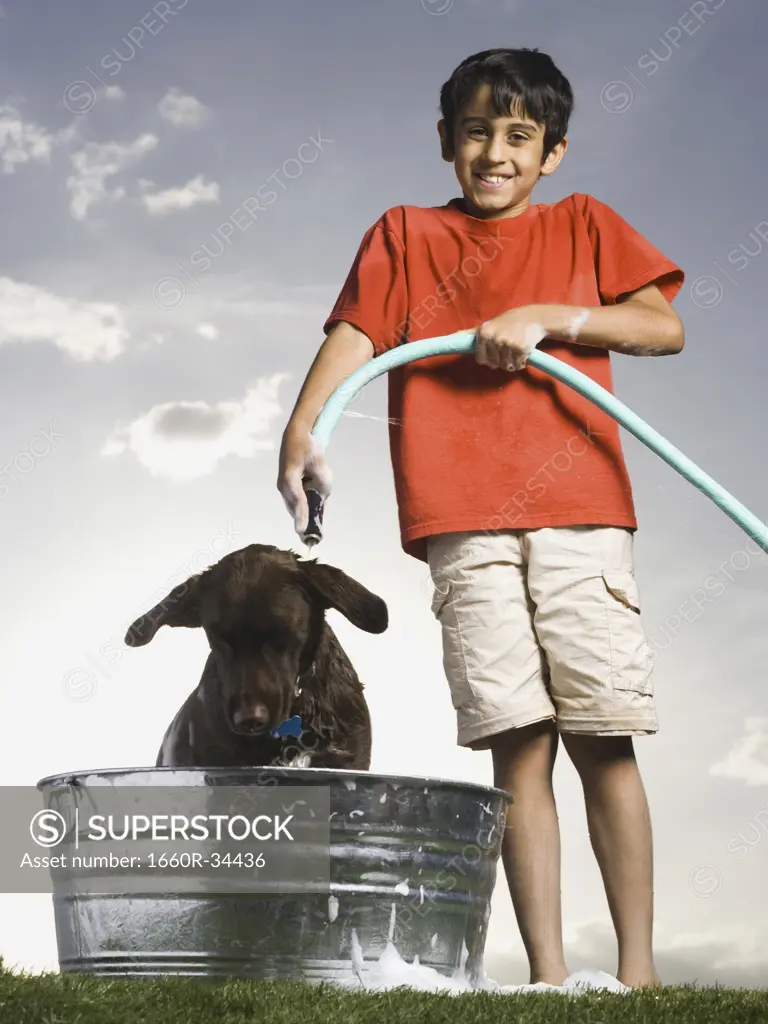 Boy bathing dog outdoors on cloudy day smiling