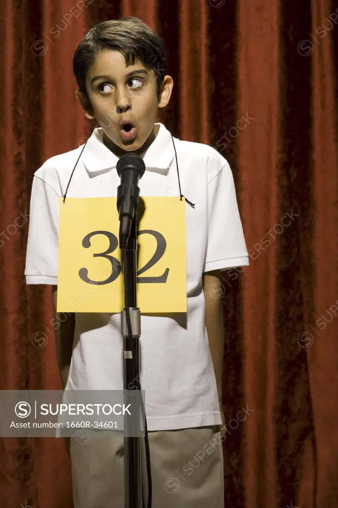 Boy standing at microphone speaking with number around neck