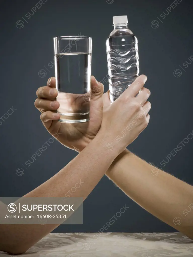 Hand holding glass of water and hand holding bottled water intertwined