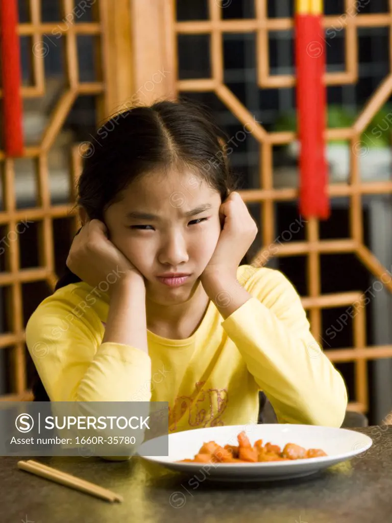 Girl sitting at table looking at plate of food with disgust