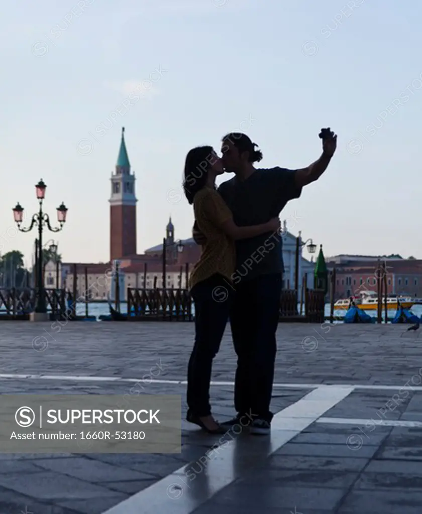 Italy, Venice, Young couple kissing and photographing self, San Giorgio Maggiore church in background