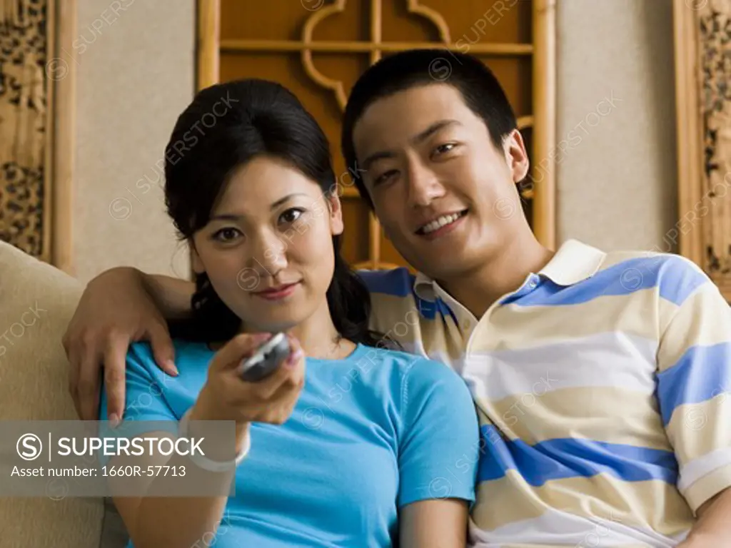 Couple embracing on sofa while woman changes channels with television remote