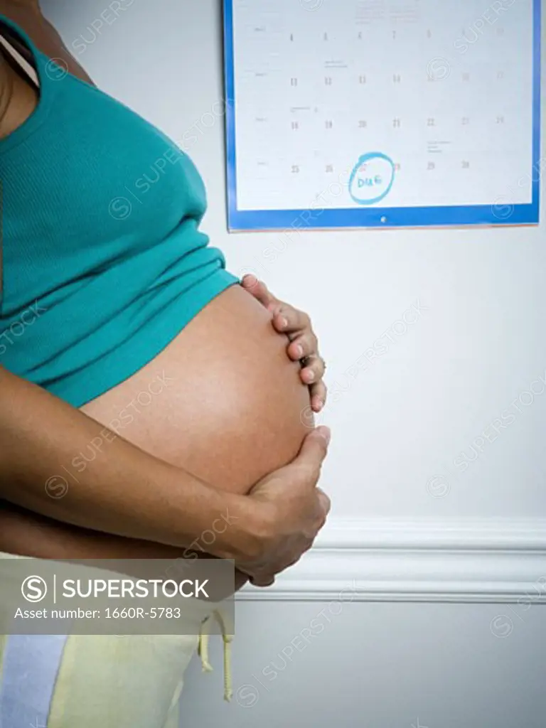 Profile of a pregnant woman touching her stomach in front of a calendar