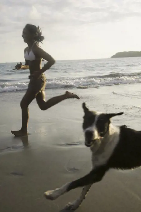 Profile of a young woman and her dog running on the beach