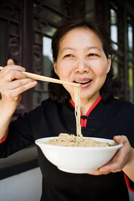 Woman with bowl of noodles and chopsticks eating