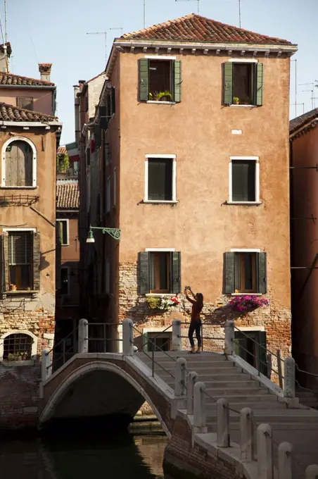 Italy, Venice, Woman standing on arch bridge and photographing italian houses