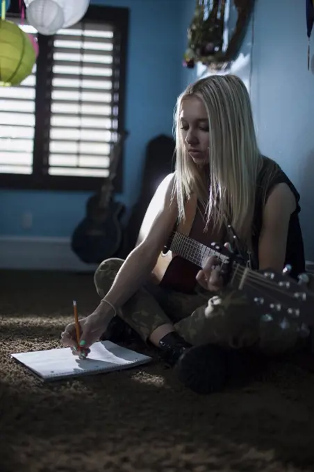 Concentrating musician writing music with acoustic guitar sitting cross legged on floor