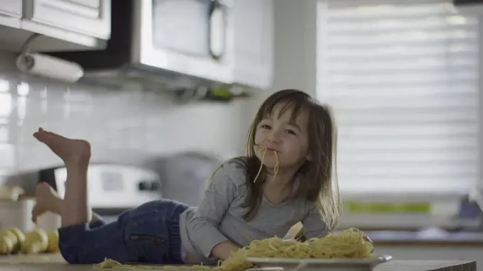 Naughty messy girl laying on kitchen counter eating plate of spaghetti