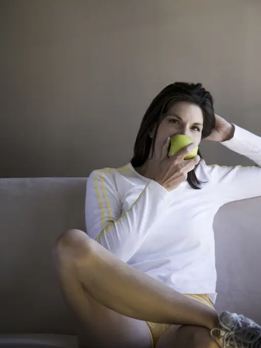 Woman sitting on sofa eating green apple