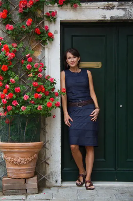 Italy, Venice, Mature woman standing against old doors, potted red roses on side