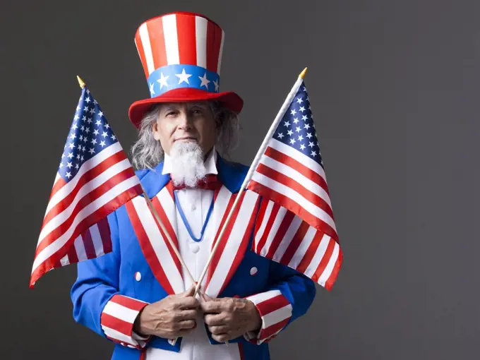 Man in Uncle Sam's costume holding american flags, studio shot