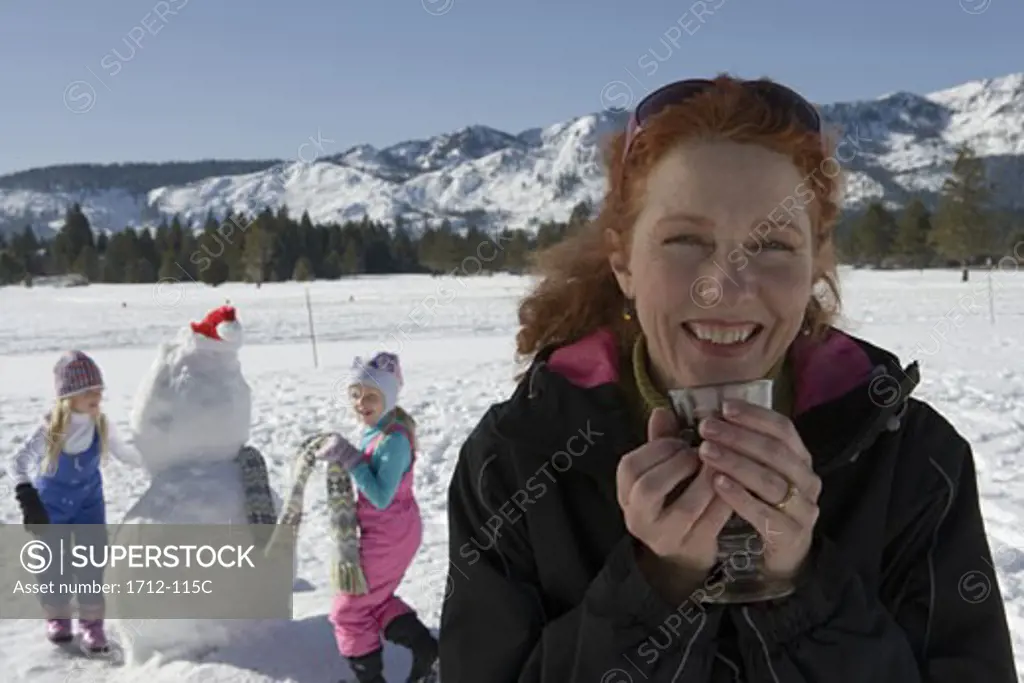 Mature woman holding a glass with her two daughters decorating a snowman